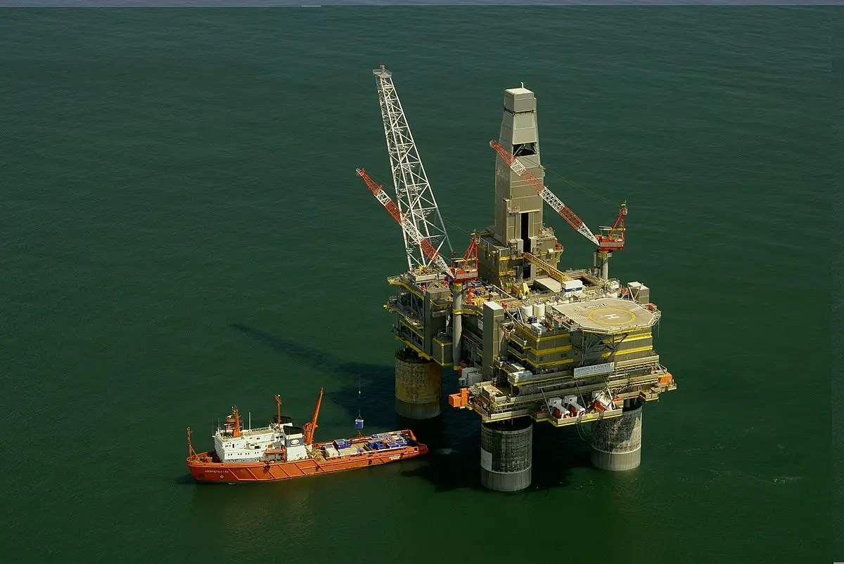 Aerial view of an offshore oil rig with a supply ship alongside, set against a calm blue ocean.