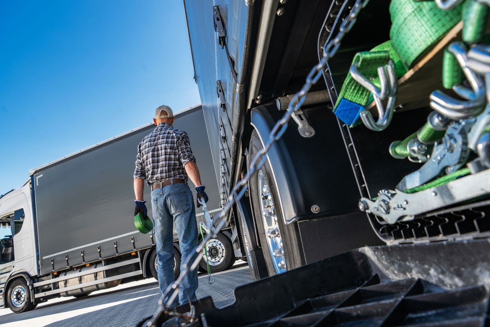 A truck driver prepares for inspection, walking beside a heavy-duty truck loaded with secured cargo straps
